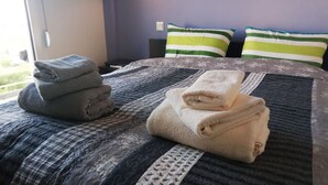 Un lit bien fait, avec une couvre-lit à motifs et deux oreillers, dont l’un est rayé et l’autre est d’un vert uni.