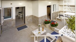 Uma área de pátio externa moderna com disposição de assentos, plantas em vasos e vista para o interior.
