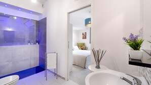 Um banheiro moderno com uma banheira grande, chuveiro separado e um quarto visível ao fundo.