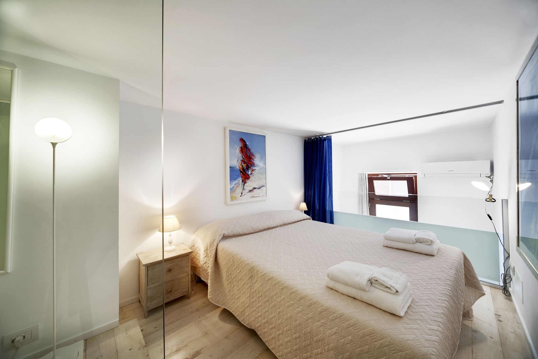 Une chambre à coucher moderne avec un lit, des lampes de chevet, un tableau et une fenêtre avec des rideaux.