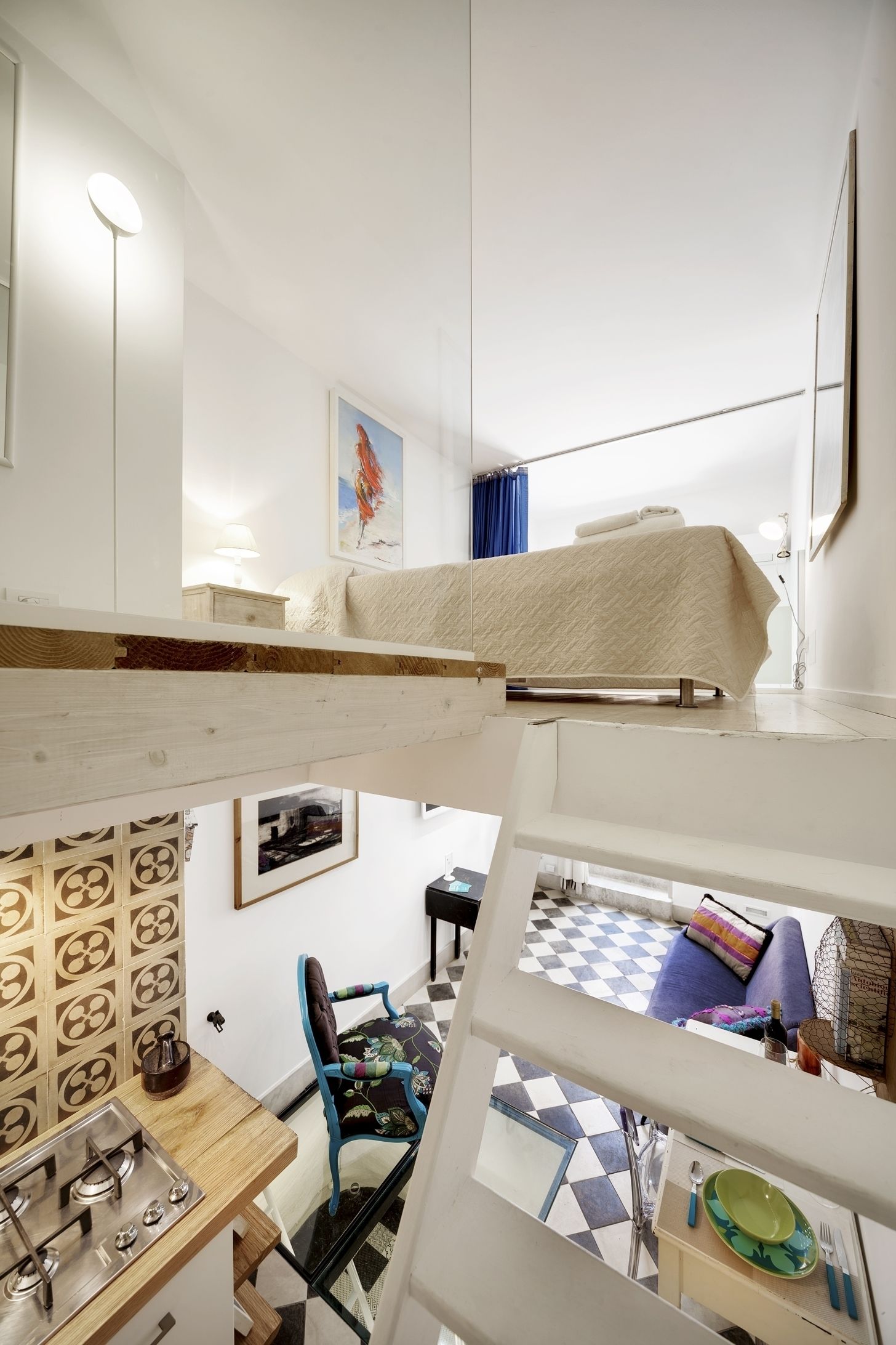 A compact hotel room with a bunk bed, a small kitchenette, a dining area, and a checkered floor.