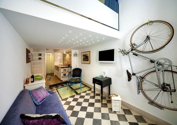 Uma sala de estar moderna com piso xadrez, um sofá azul, uma bicicleta pendurada e uma TV na parede.