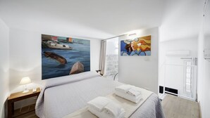 A hotel room with a bed, a nightstand with a lamp, a painting of a boat on the wall, and a window with curtains. - Marina Domus Dependance (Ragusa)