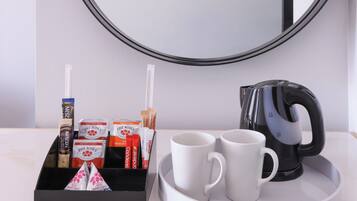 Un plateau avec deux tasses blanches, une bouilloire électrique noire et une boîte de sachets de café Nescafé Gold et Five Roses.