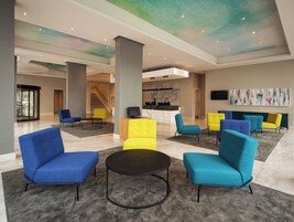 A spacious lobby with modern seating, a reception desk, and a staircase in the background.