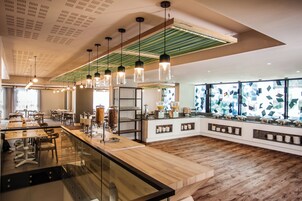 A modern restaurant with a long counter, hanging pendant lights, and a geometric patterned window.