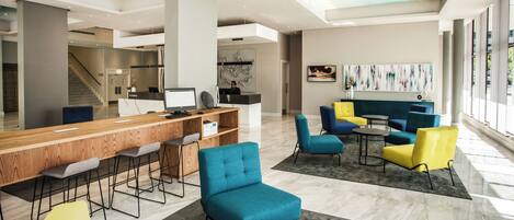 A modern lobby with a reception desk, bar seating, and colorful chairs.