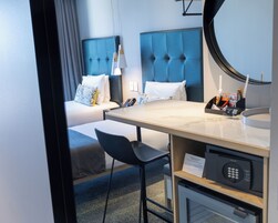 A hotel room with a bed, a desk, a chair, a round mirror, and a minibar.