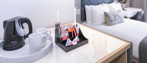 Habitación de hotel con cama, mesita de noche y bandeja con cafetera, tazas y artículos de aseo.