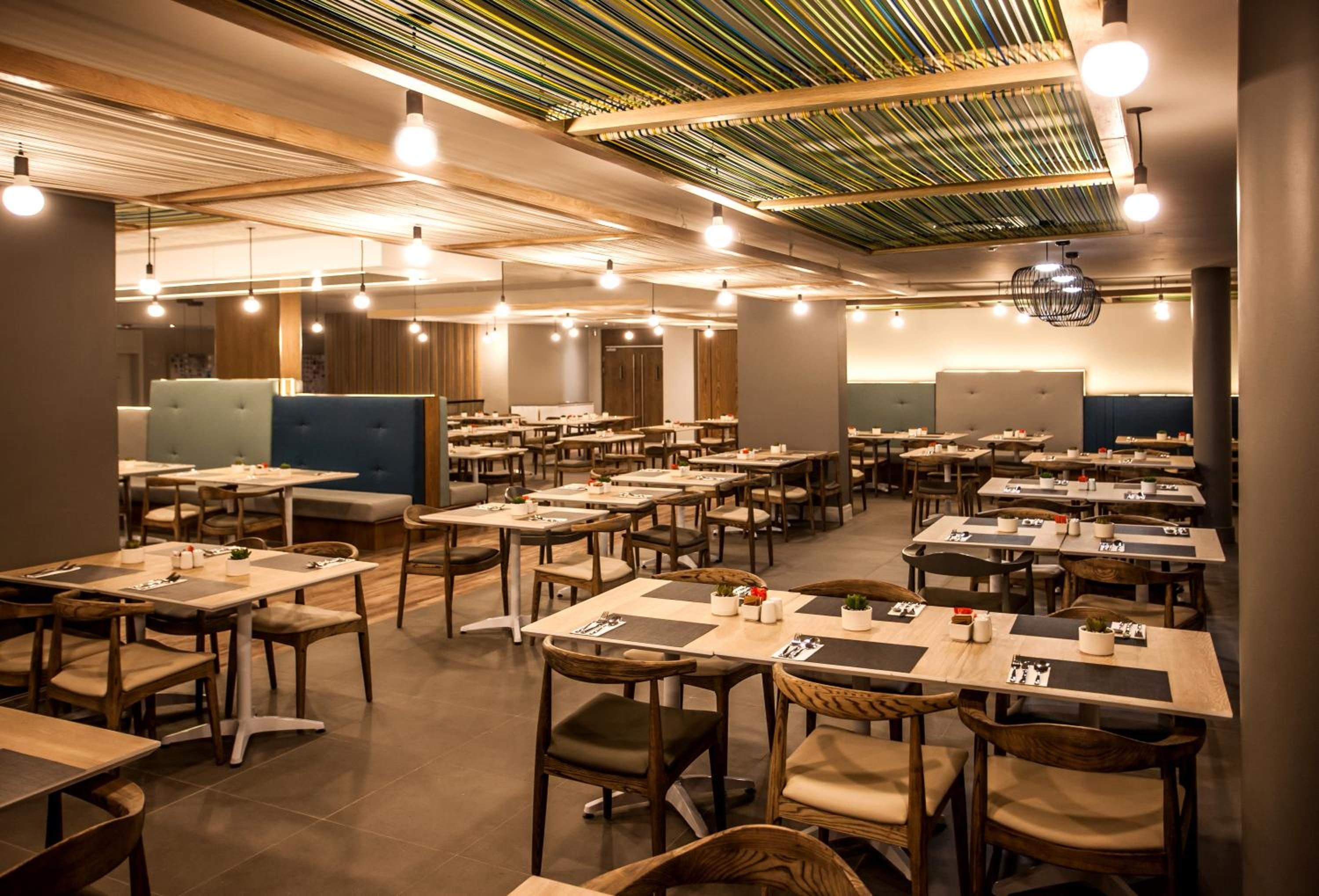Un restaurant spacieux, doté de nombreuses tables et de banquettes, d’un plancher en bois et d’un plafond avec des poutres apparentes et des luminaires suspendus.