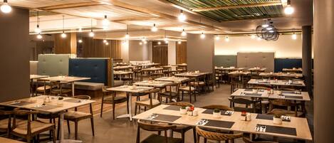 A spacious restaurant with multiple tables and booths, wooden flooring, and a ceiling with exposed beams and hanging lights.