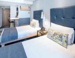 A modern hotel room with two beds, a desk, and a chair.