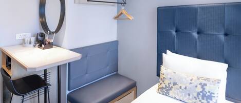 A modern hotel room with a bed, a bench, a desk, and a mirror.