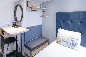 A modern hotel room with a bed, a bench, a desk, and a mirror.