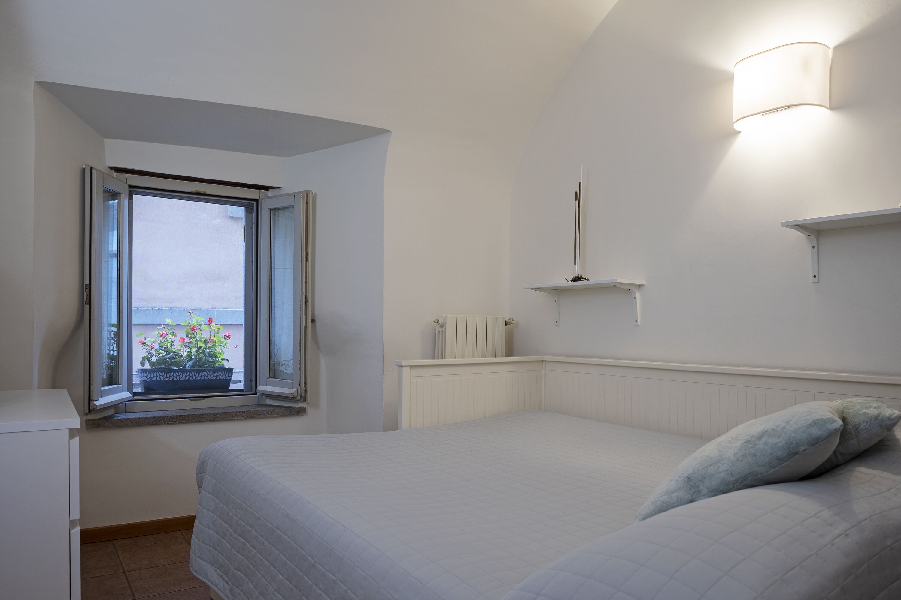 Una camera da letto con un letto, una finestra con persiane aperte, un termosifone e un lampadario a parete.