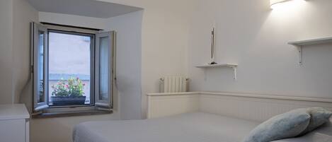 A bedroom with a bed, a window with open shutters, a radiator, and a wall-mounted light fixture.