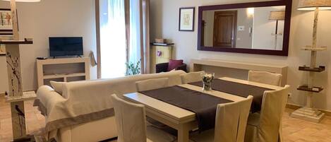 A modern living room with a dining area, a TV, a large mirror, and a cat tree.