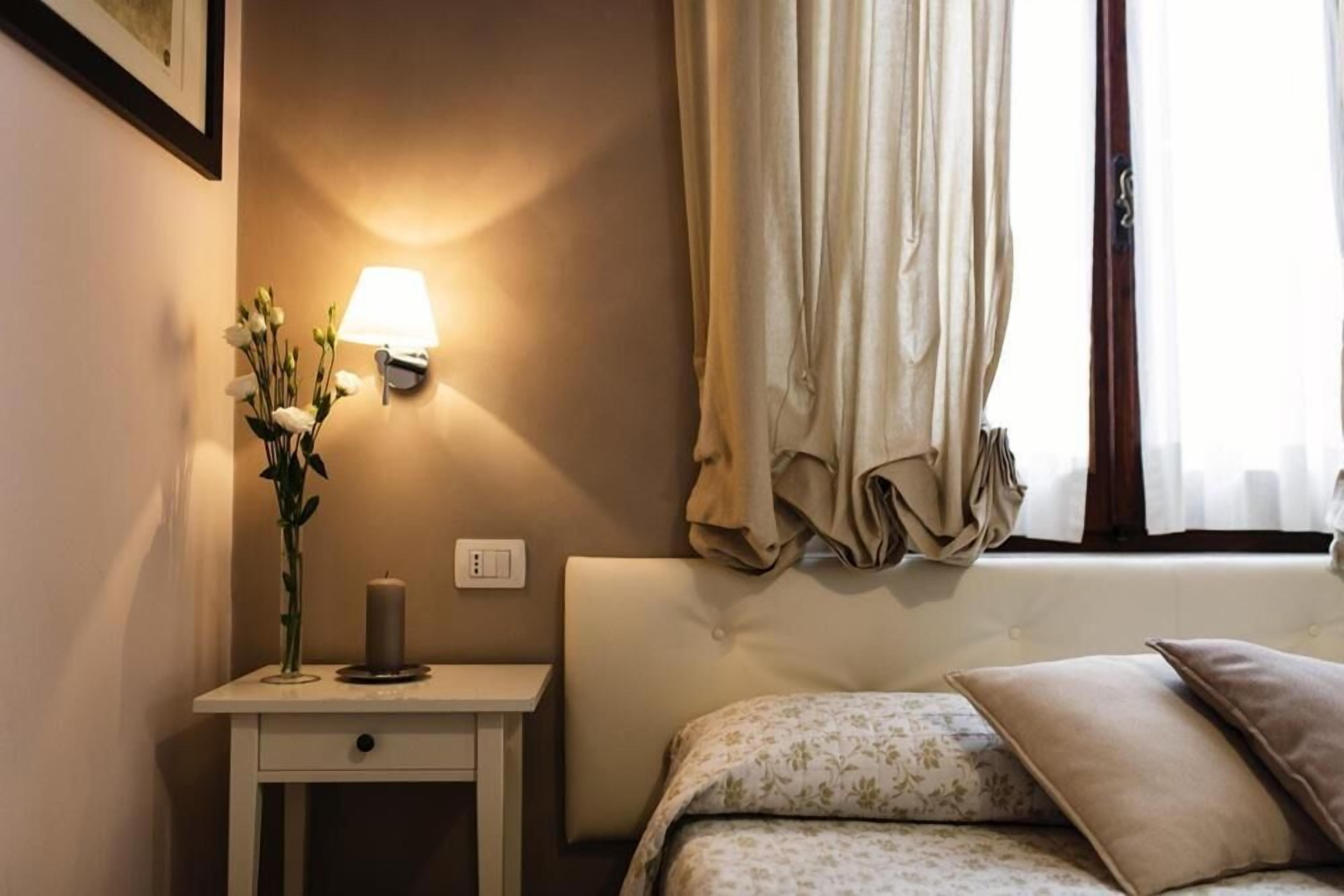 Une chambre à coucher bien rangée, avec un lit, une table de chevet dotée d’une lampe et un vase rempli de fleurs.