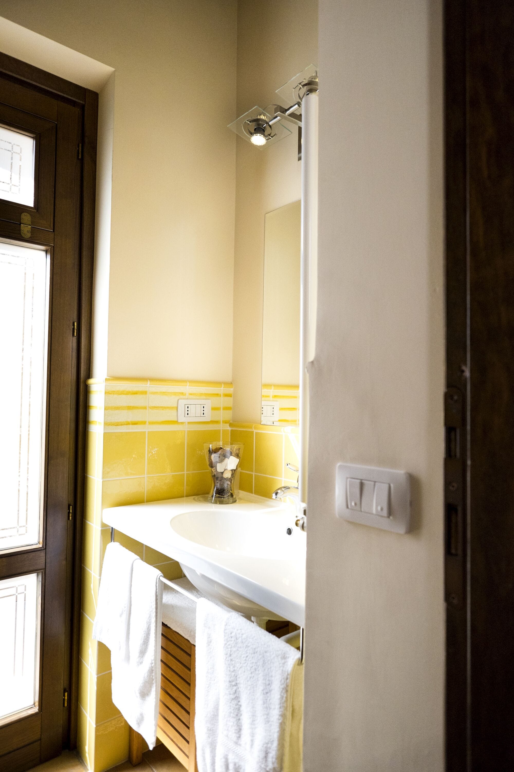 A bathroom with a yellow and white tiled wall, a white sink, and a mirror above it.