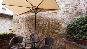 Une terrasse en pierre avec deux fauteuils en osier et une table placée sous un grand parasol.