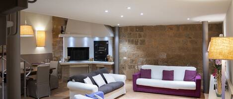 A modern living room with a sofa, a dining area with chairs, and a kitchen with a stove and oven.