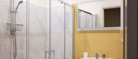 A bathroom with a glass-enclosed shower, a white sink, and a mirror above it.