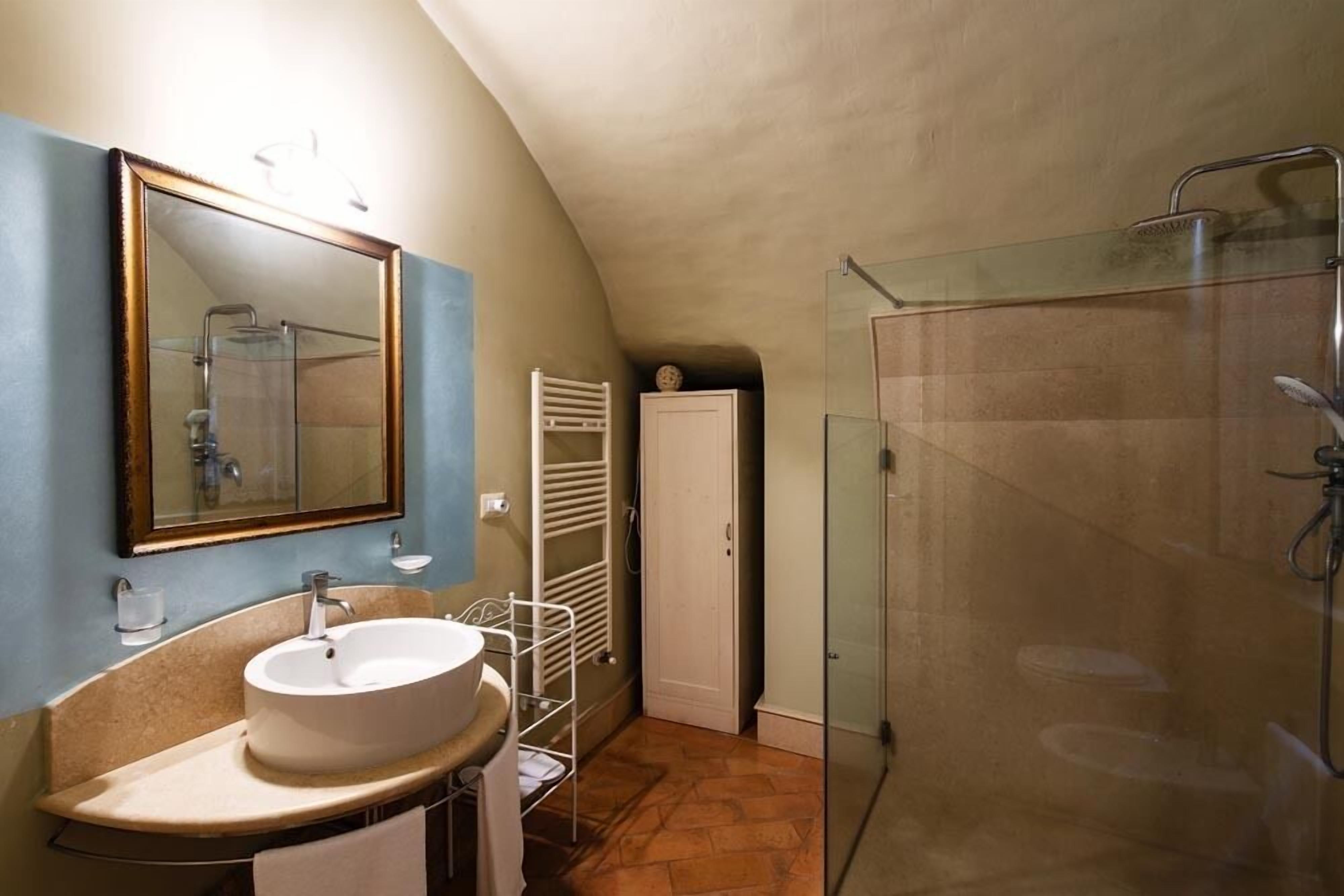 A bathroom with a round sink, a mirror, a glass shower enclosure, and a towel rack.