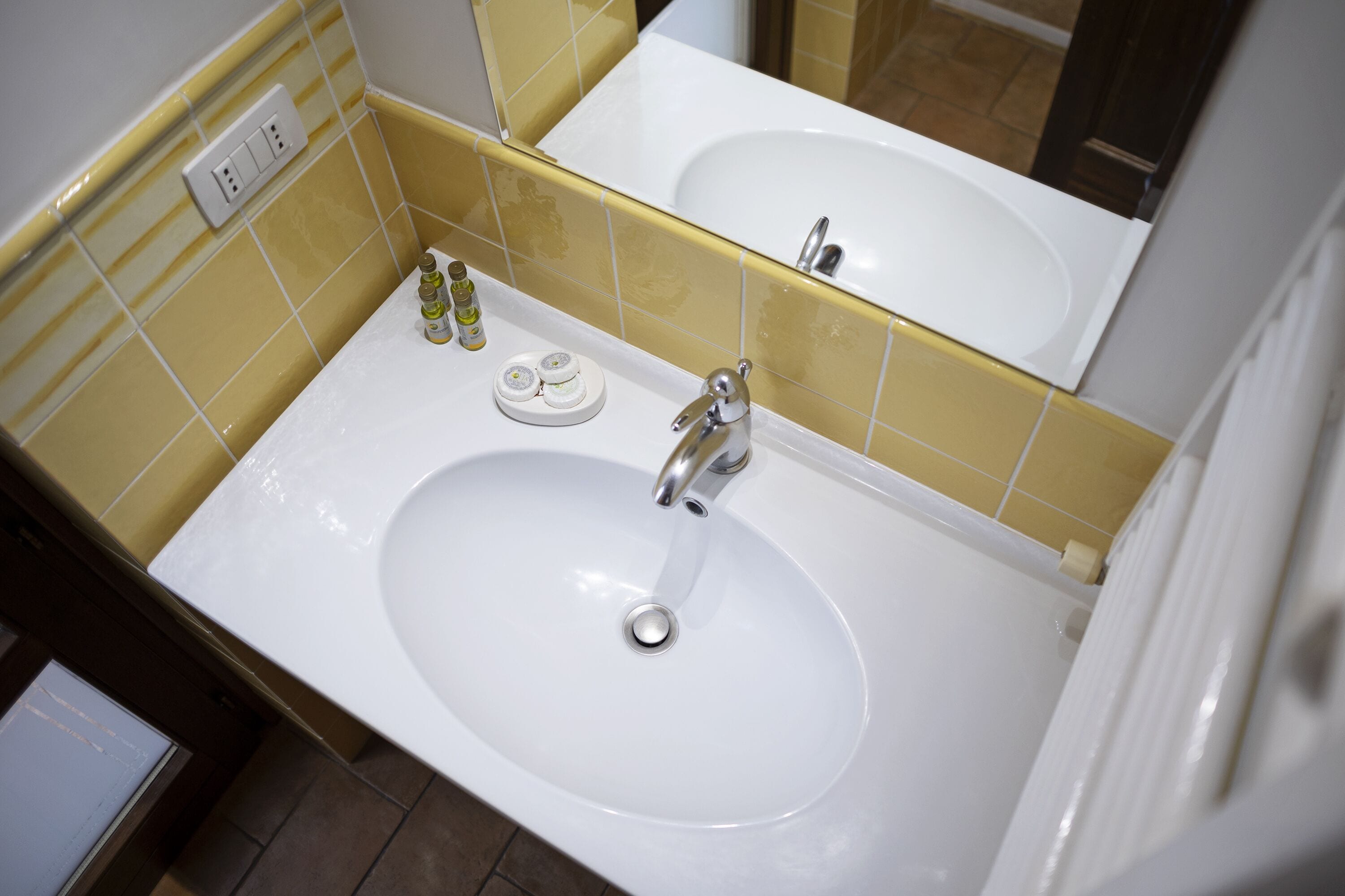 Ein Badezimmer mit weißem Waschbecken, gelb gefliesten Wänden, einem Spiegel und einer weißen Arbeitsplatte.