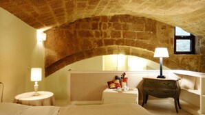Une chambre avec un plafond voûté en pierre, un lit, une table de chevet avec une lampe, une commode et une petite fenêtre.