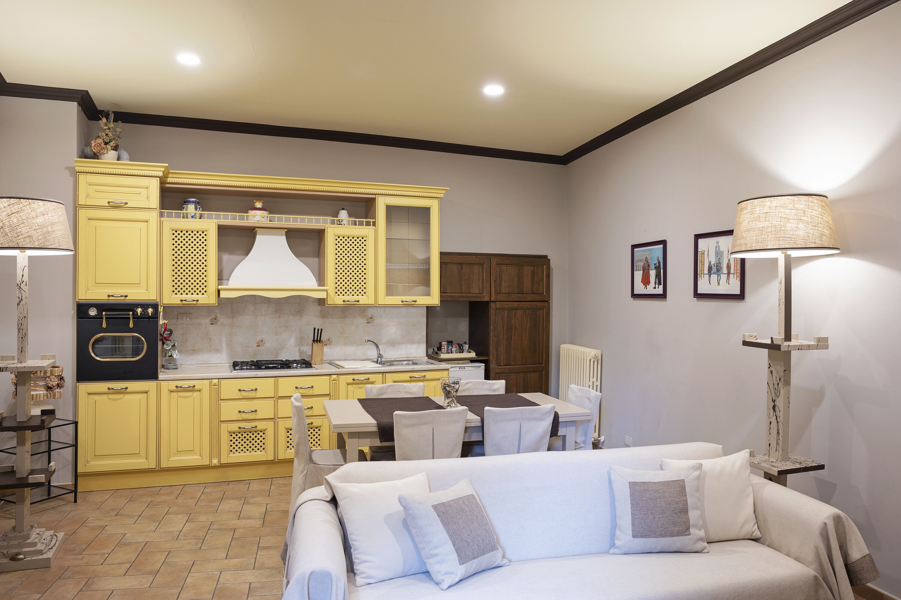 A modern kitchen with yellow cabinets, a dining area with a table and chairs, and a white sofa in the foreground.