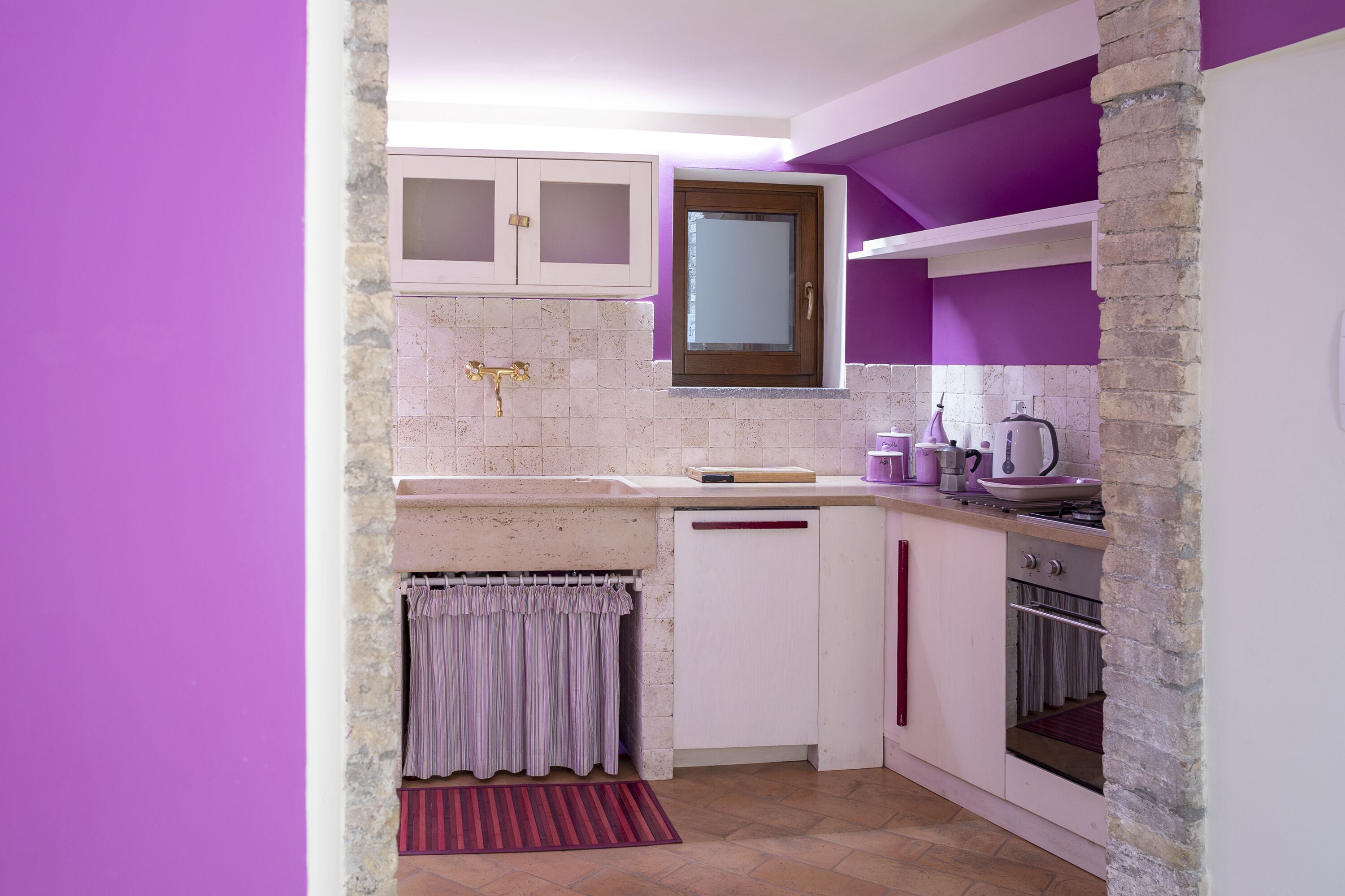 A compact kitchen with white cabinets, a built-in oven, and a window above the sink.