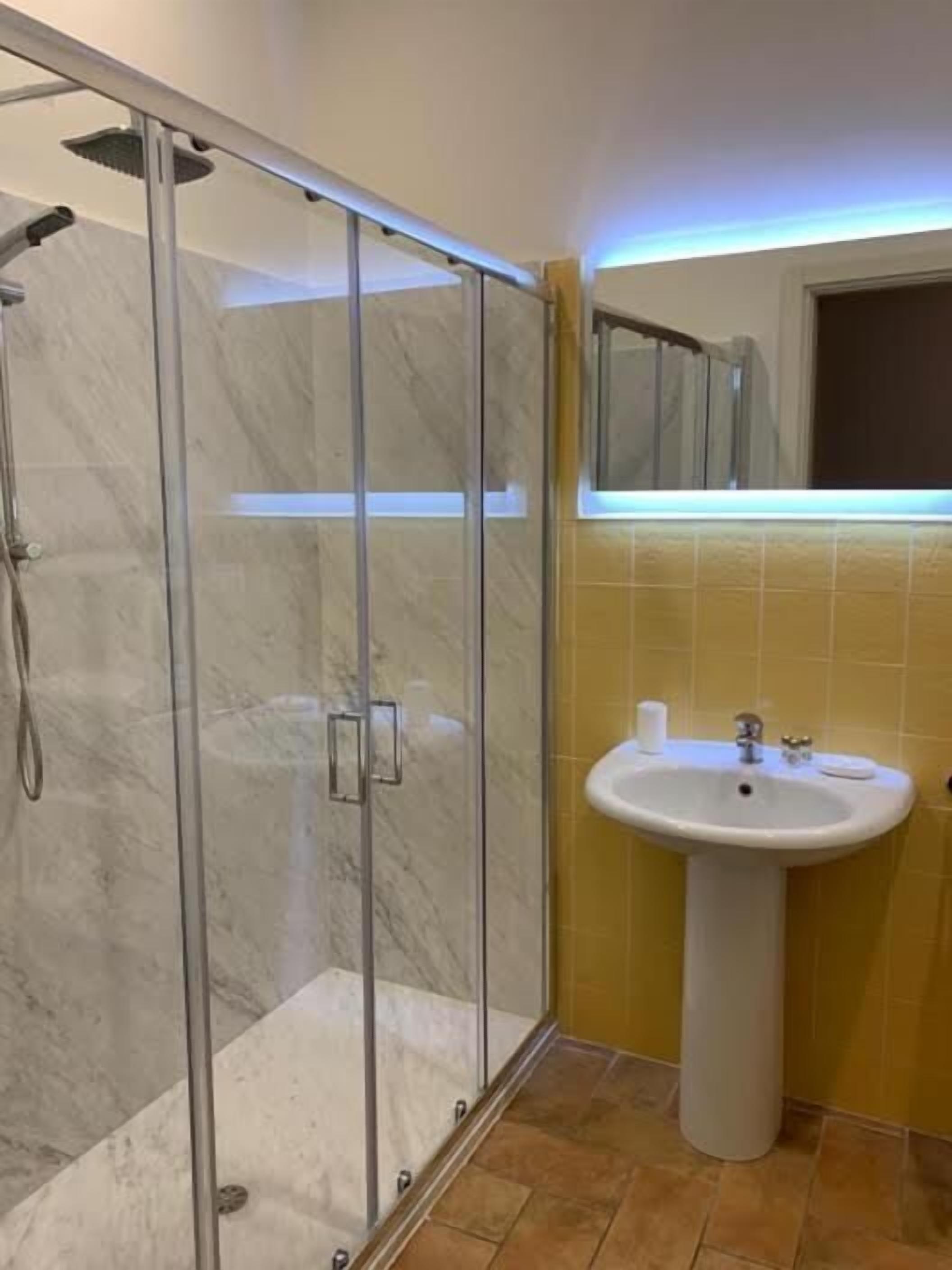 A bathroom with a glass-enclosed shower, a sink, and yellow-tiled walls.