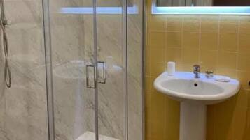 A bathroom with a glass-enclosed shower, a sink, and yellow-tiled walls.