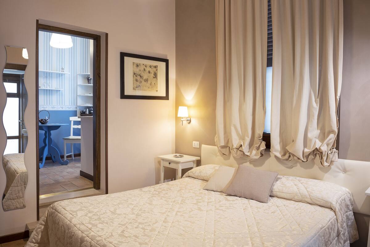 Hotelkamer met een groot bed, nachtkastje, spiegel, een wandlamp en uitzicht op de aangrenzende kamer.