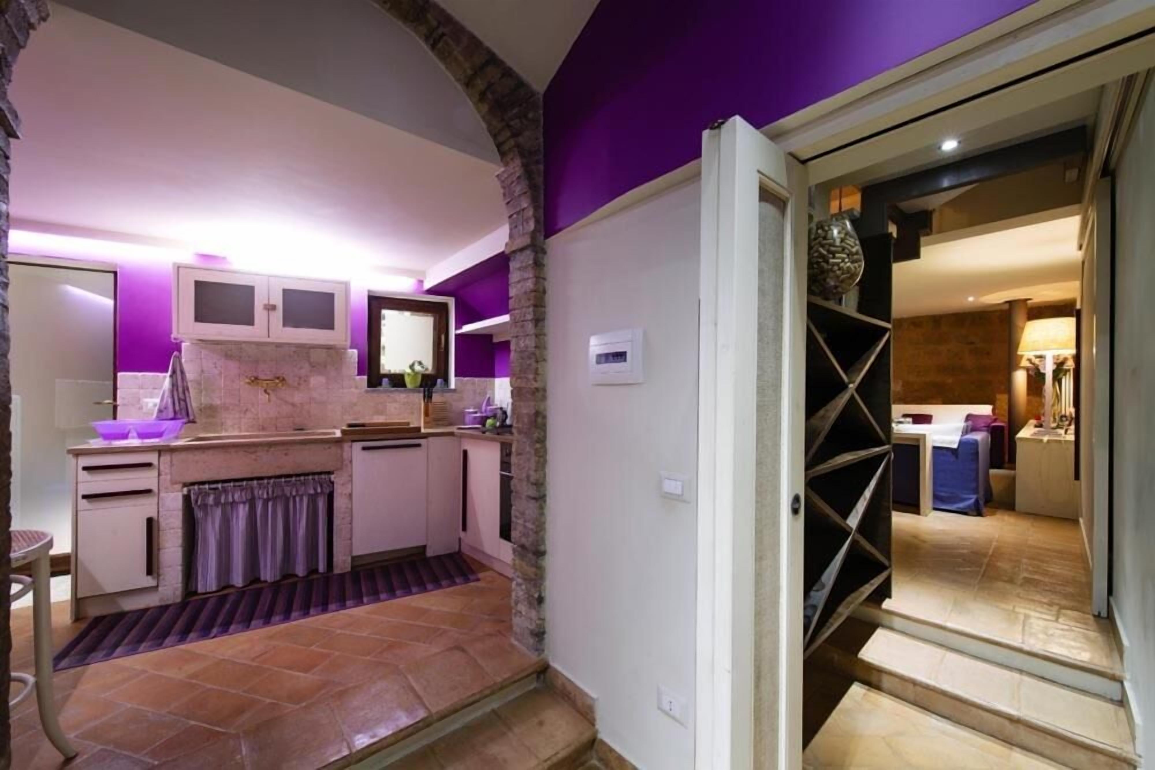 Una cocina moderna con encimera de piedra, horno empotrado y una pared de acento morada.
