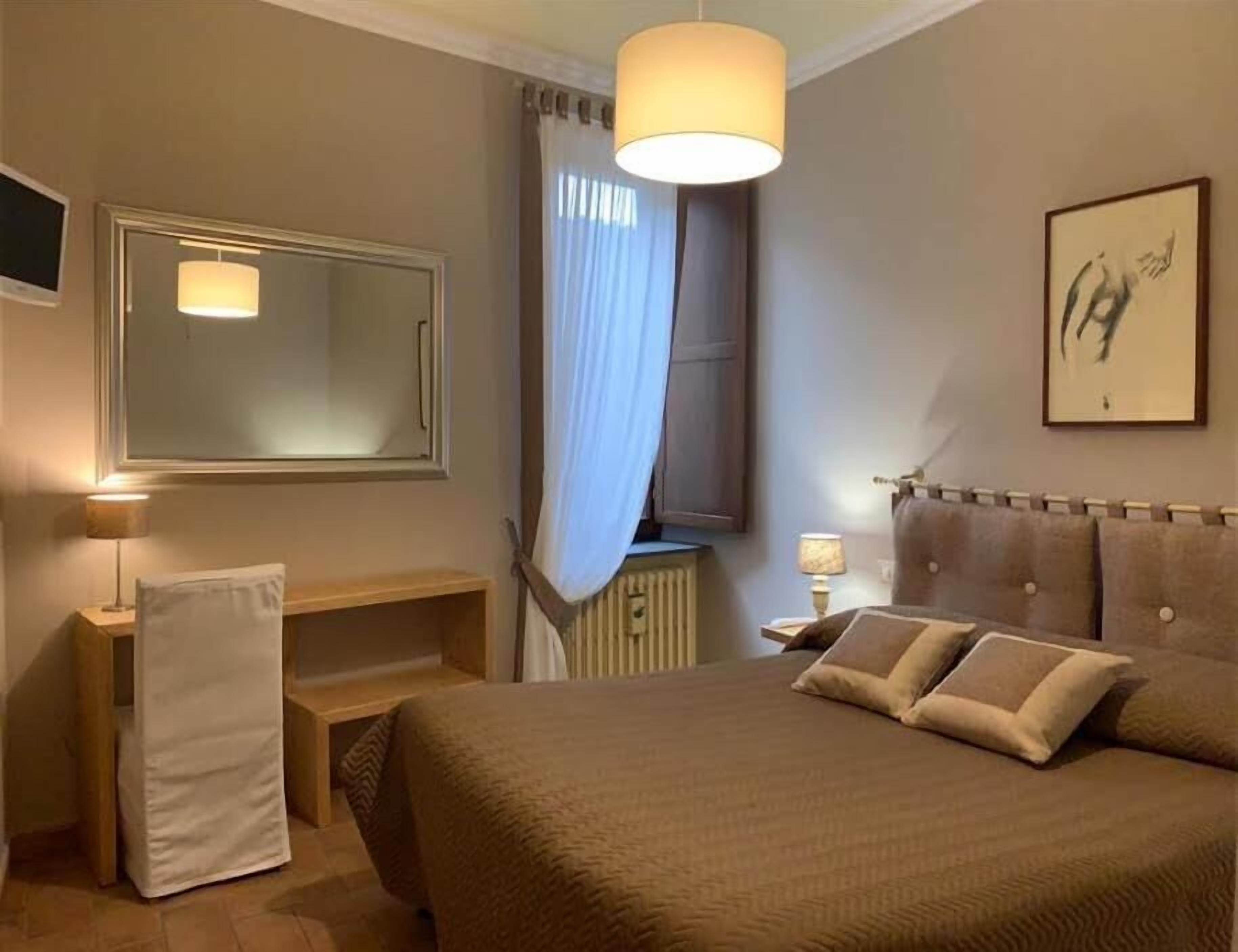 A hotel room with a large bed, bedside tables, a mirror, a radiator, and a painting on the wall.