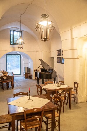 Un comedor con piano, mesas, sillas y una lámpara de araña.