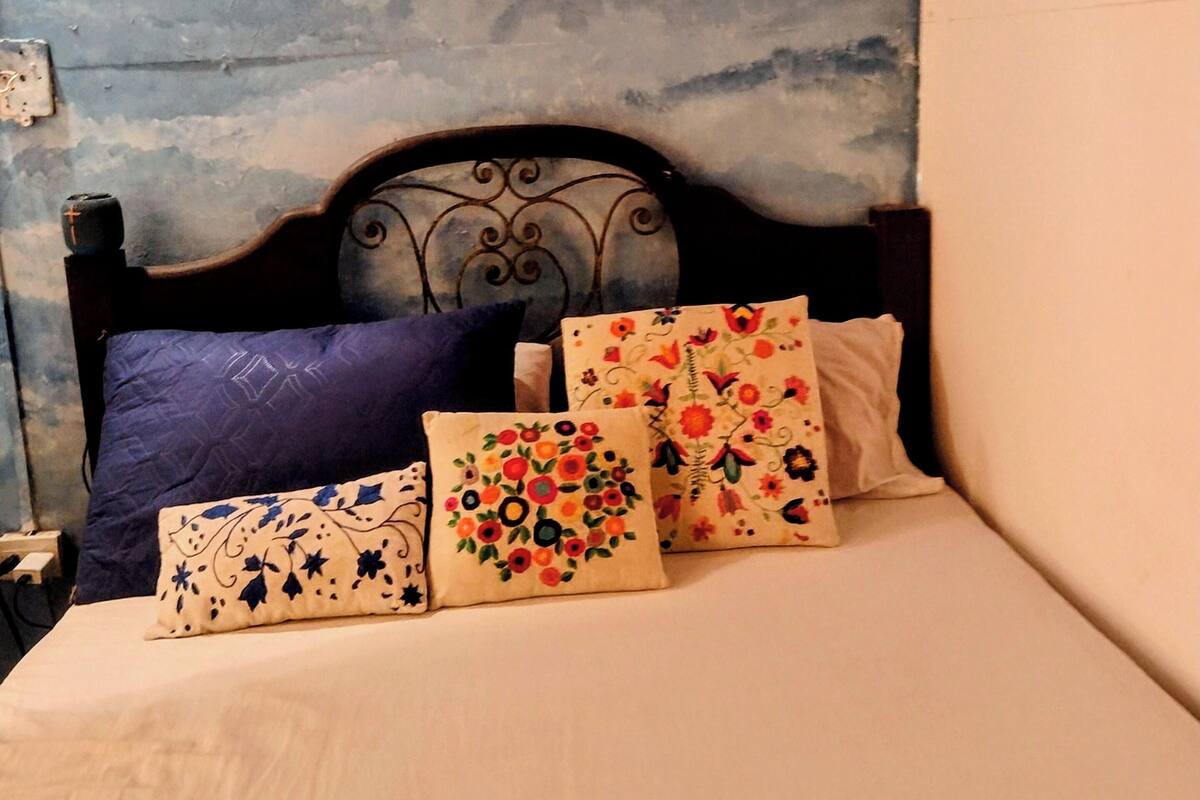 Un lit avec quatre oreillers, une tête de lit et un appareil de climatisation fixé au mur.