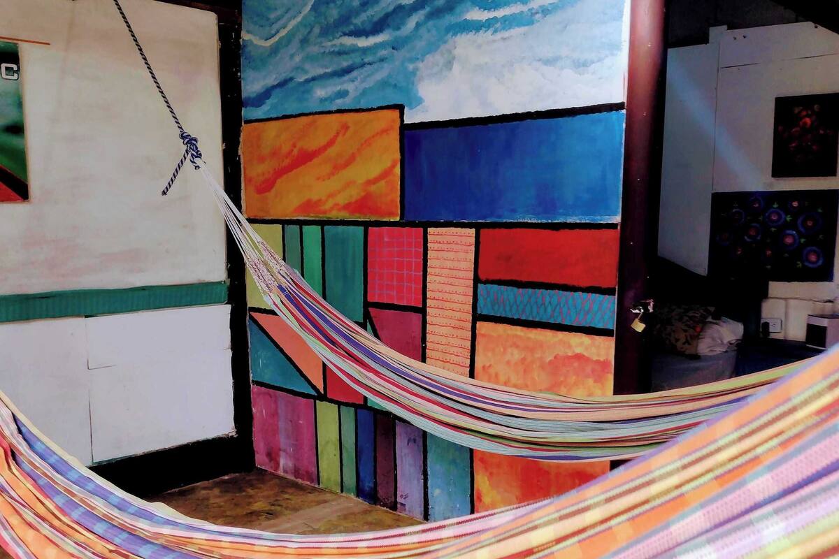 Un hamac dans une pièce aux murs colorés, dont on peut voir la structure du plafond.