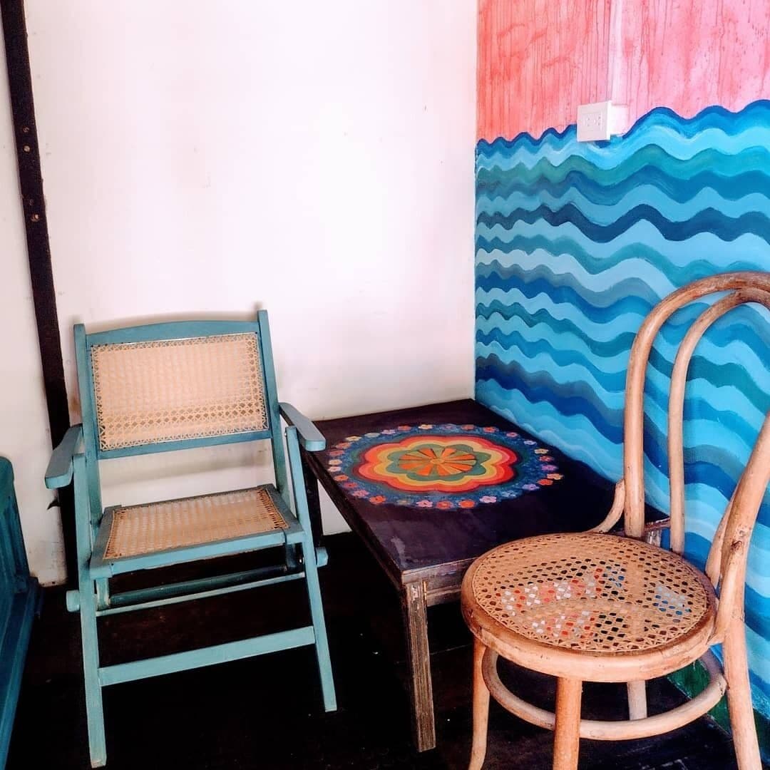 Un rincón con una silla azul turquesa, una mesita con un estampado colorido y una silla de madera.