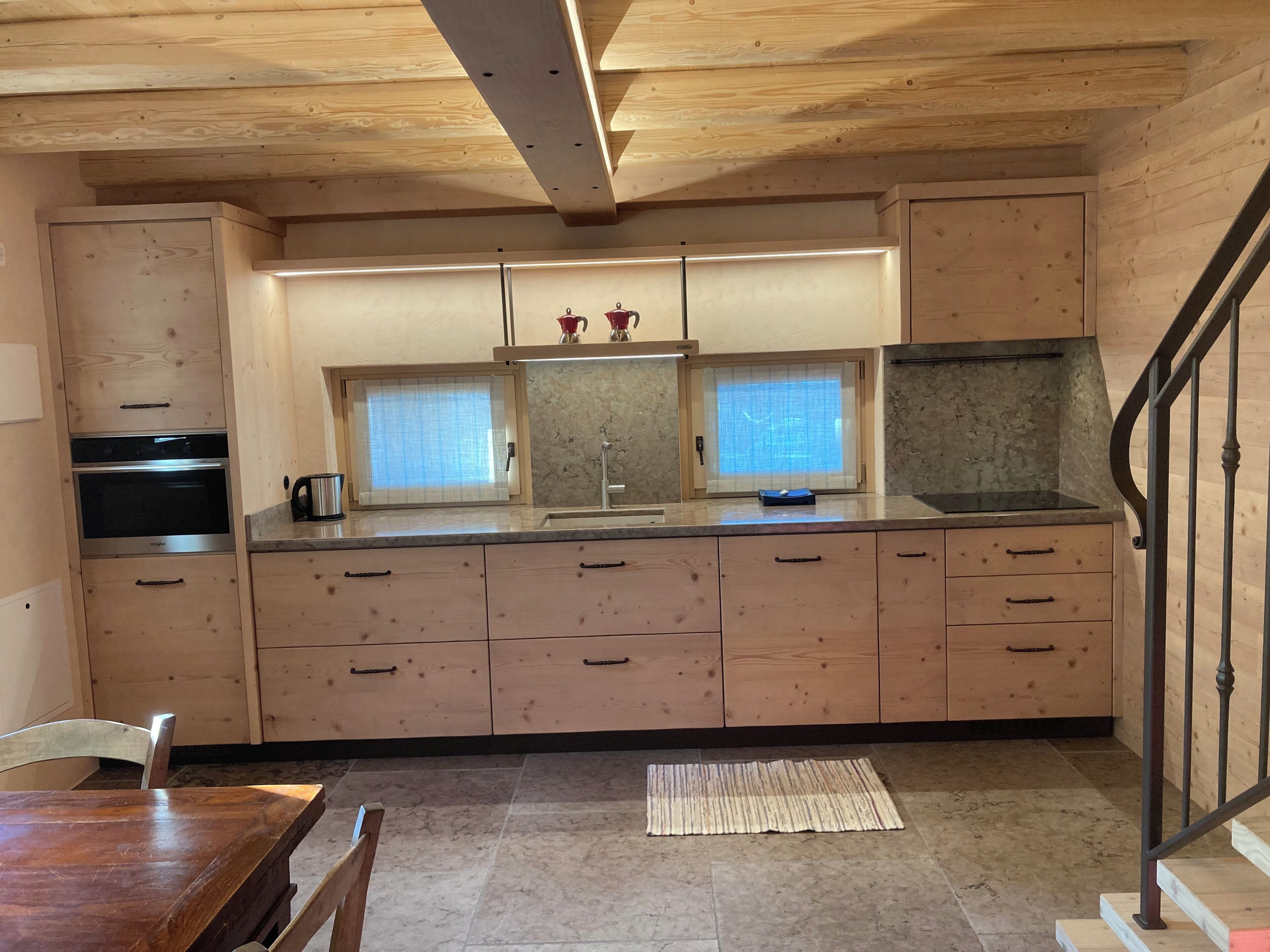 Une cuisine en bois dotée d’appareils électroménagers intégrés, d’une fenêtre et d’un escalier.
