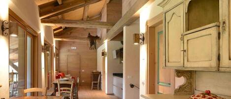 A rustic wooden interior with exposed beams, a dining area with wooden chairs and a table, and a kitchen with vintage cabinets.