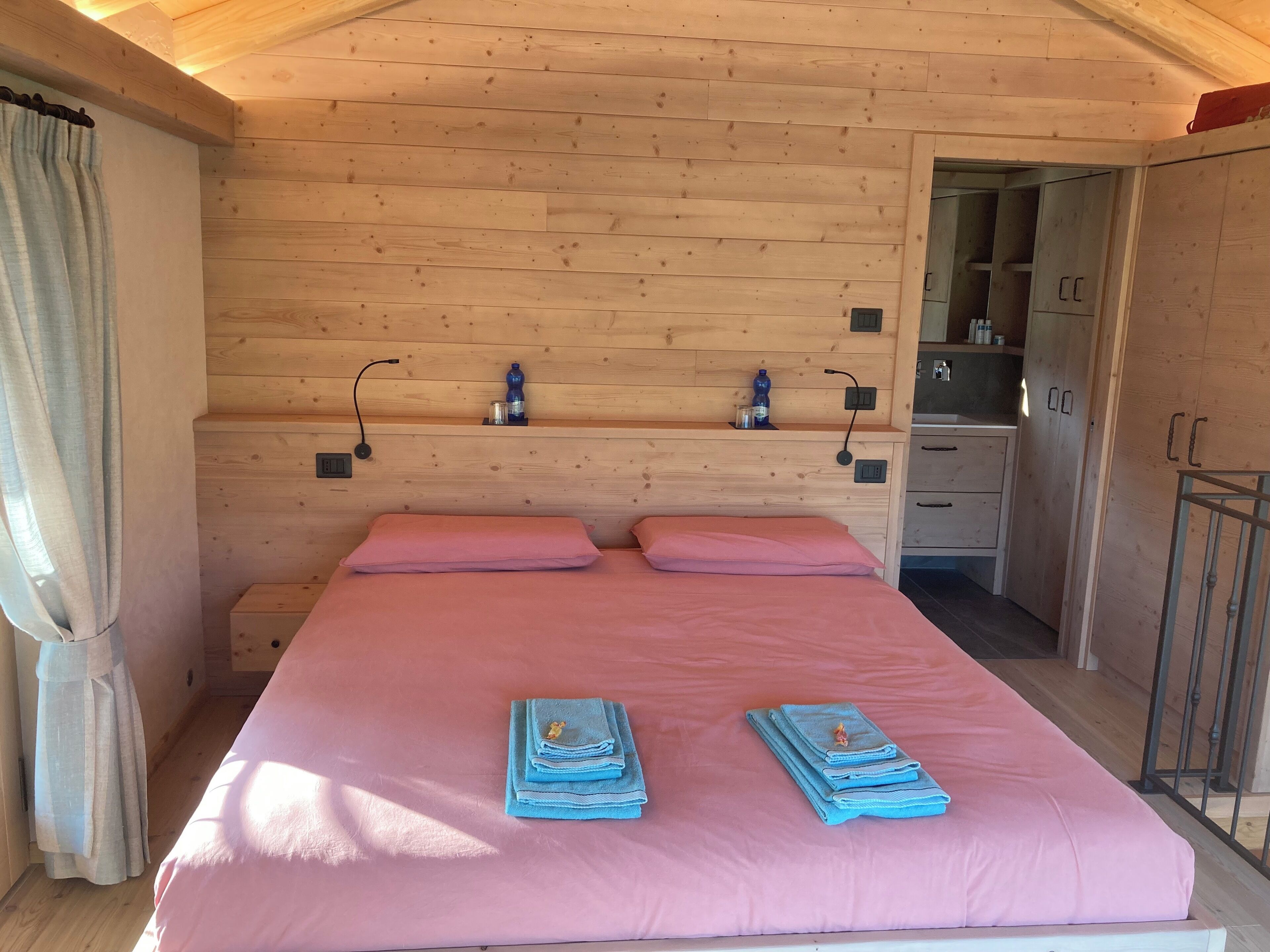 Ein Zimmer mit Holzwänden, einem Bett, einer kleinen Küchenzeile und einem durchgehenden Türspalt sichtbaren Badezimmer.