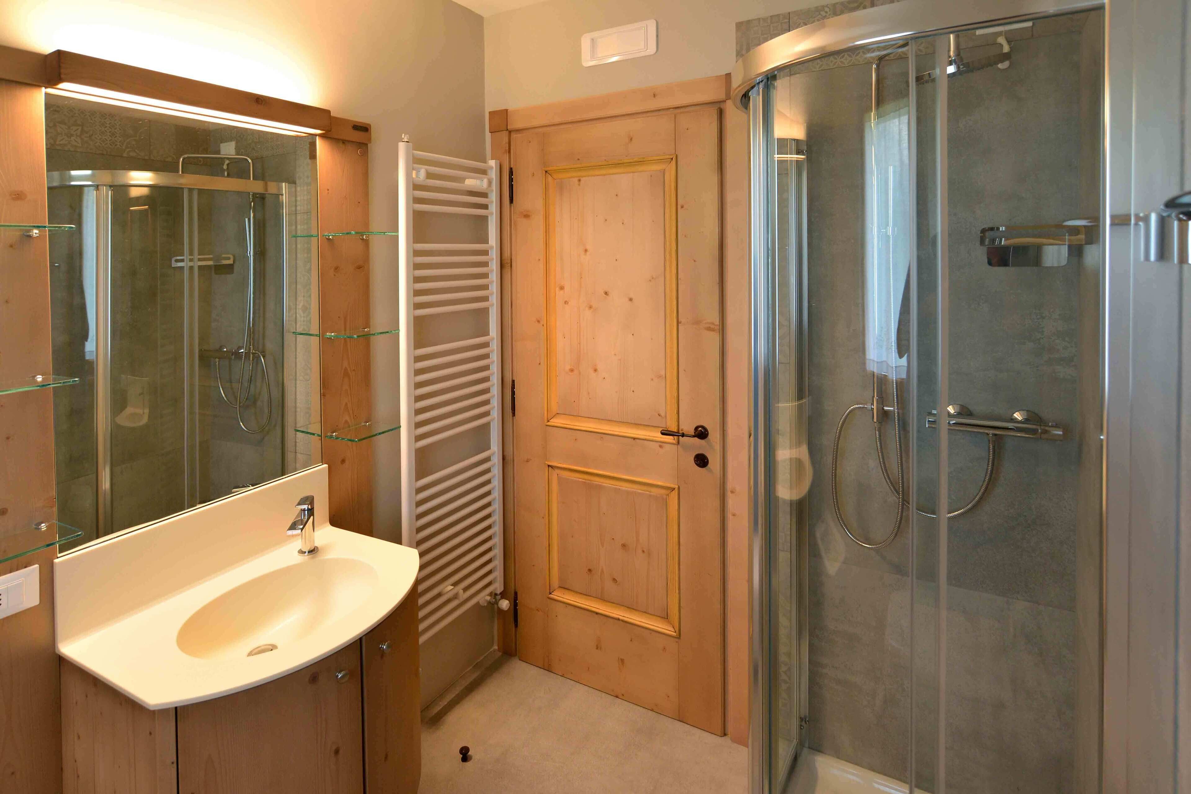 Un baño con puerta de madera, cabina de ducha con mampara de vidrio y lavabo con espejo.