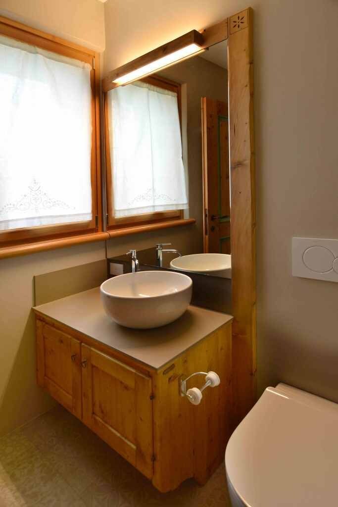 A bathroom with a wooden vanity, two sinks, a mirror, and a toilet.