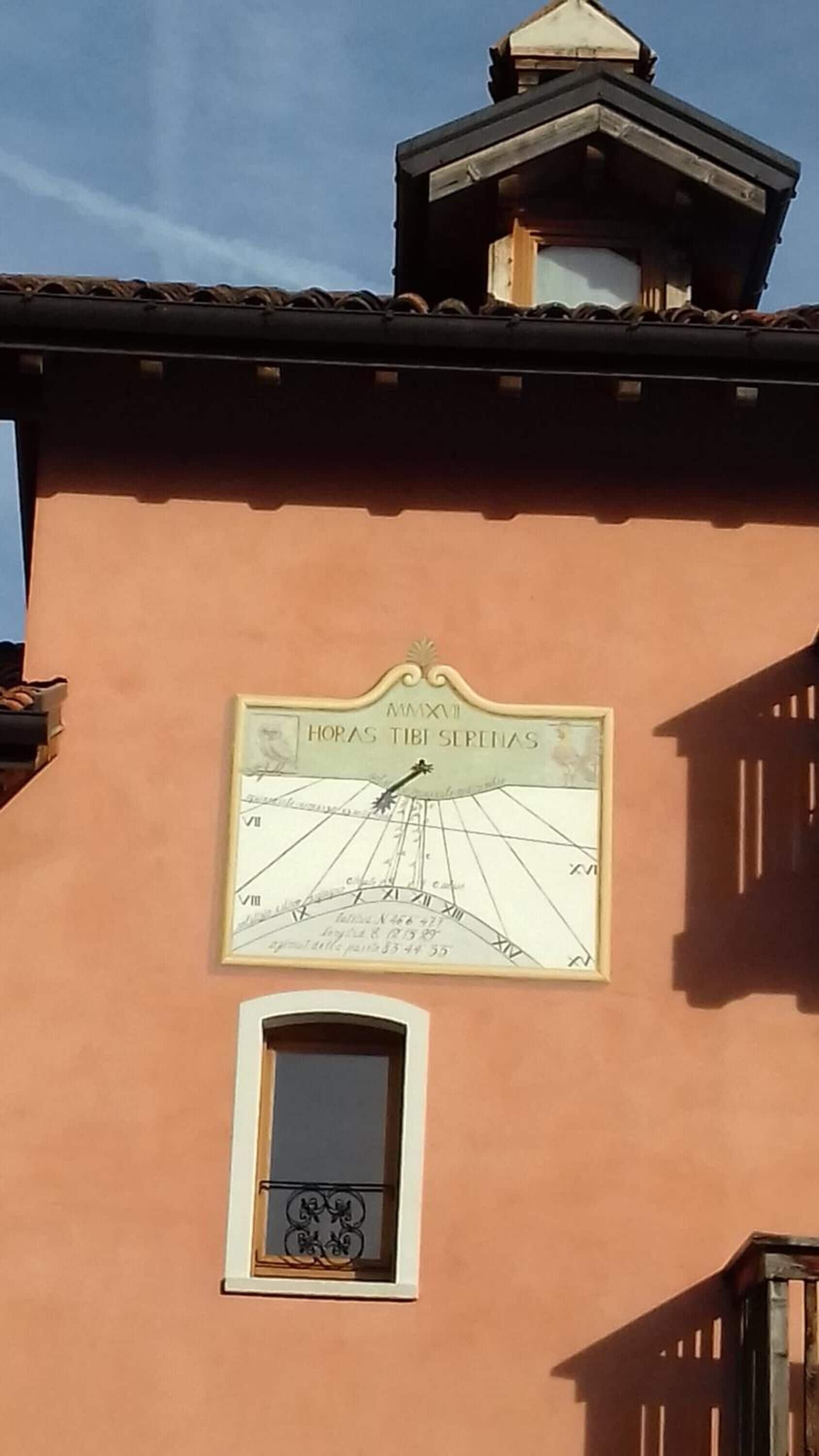 A building with a clock on the wall displaying 'HORAS TIBI SERENAS' and a small window below it.