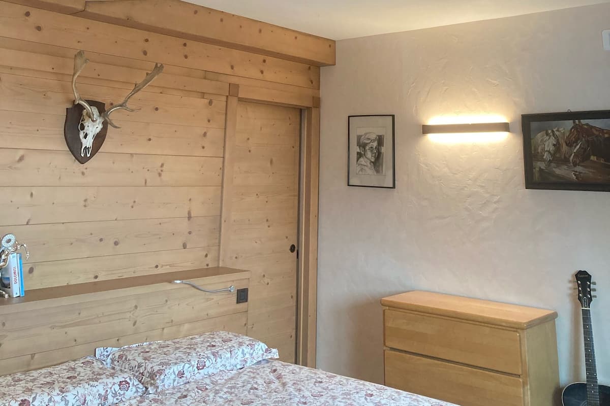 A bedroom with wooden paneling, a bed with floral bedding, a dresser, a guitar, and a wall-mounted picture.
