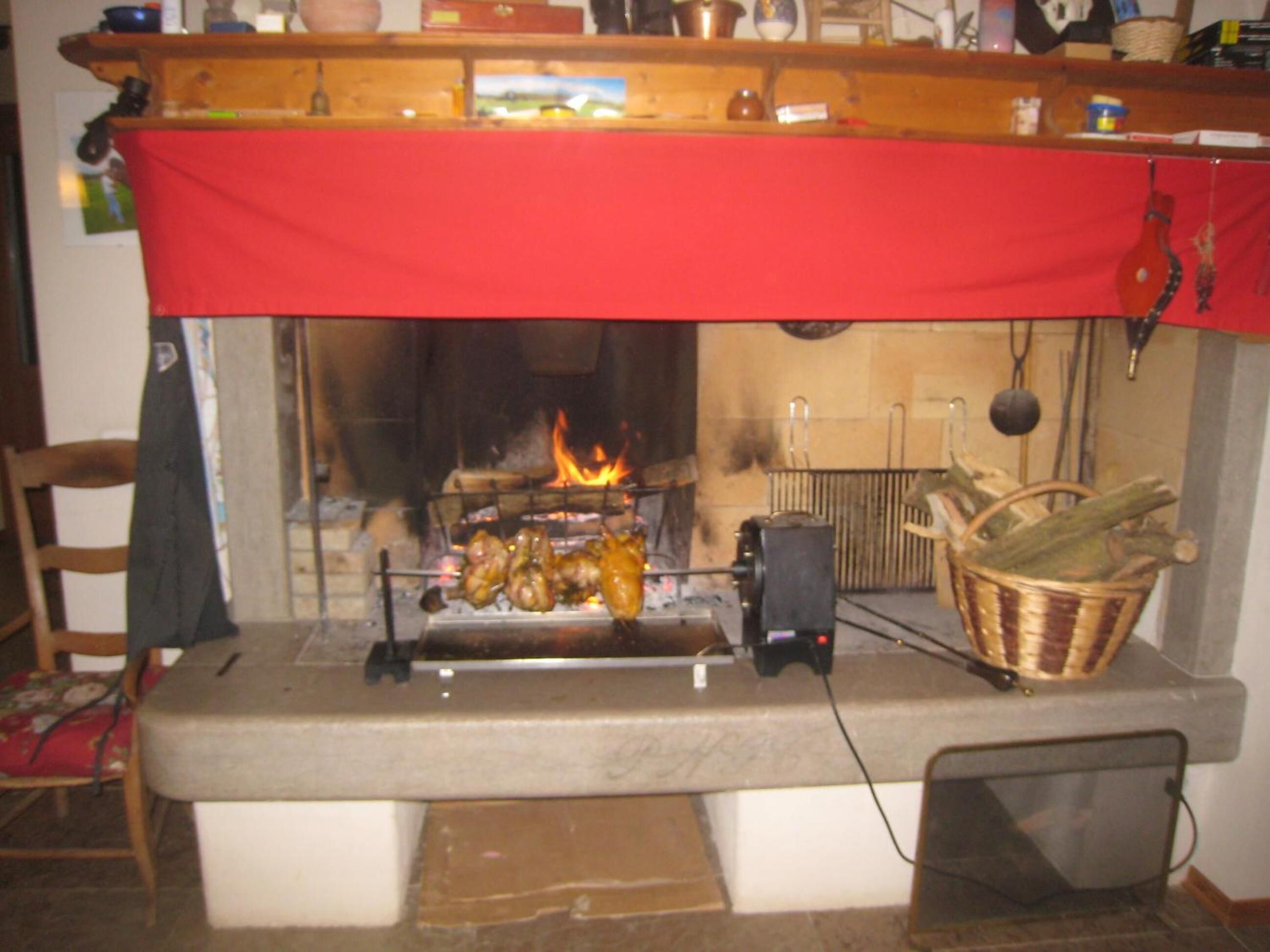 Uma cozinha com fogão a lenha, uma cesta suspensa de vegetais e um pano vermelho sobre o fogão.