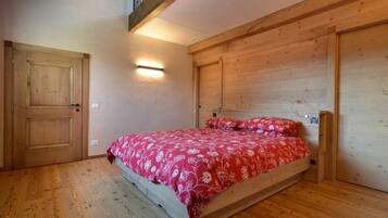 Un dormitorio con piso de madera, una cama con colcha floral roja, cabecera de madera y una lámpara de pared.