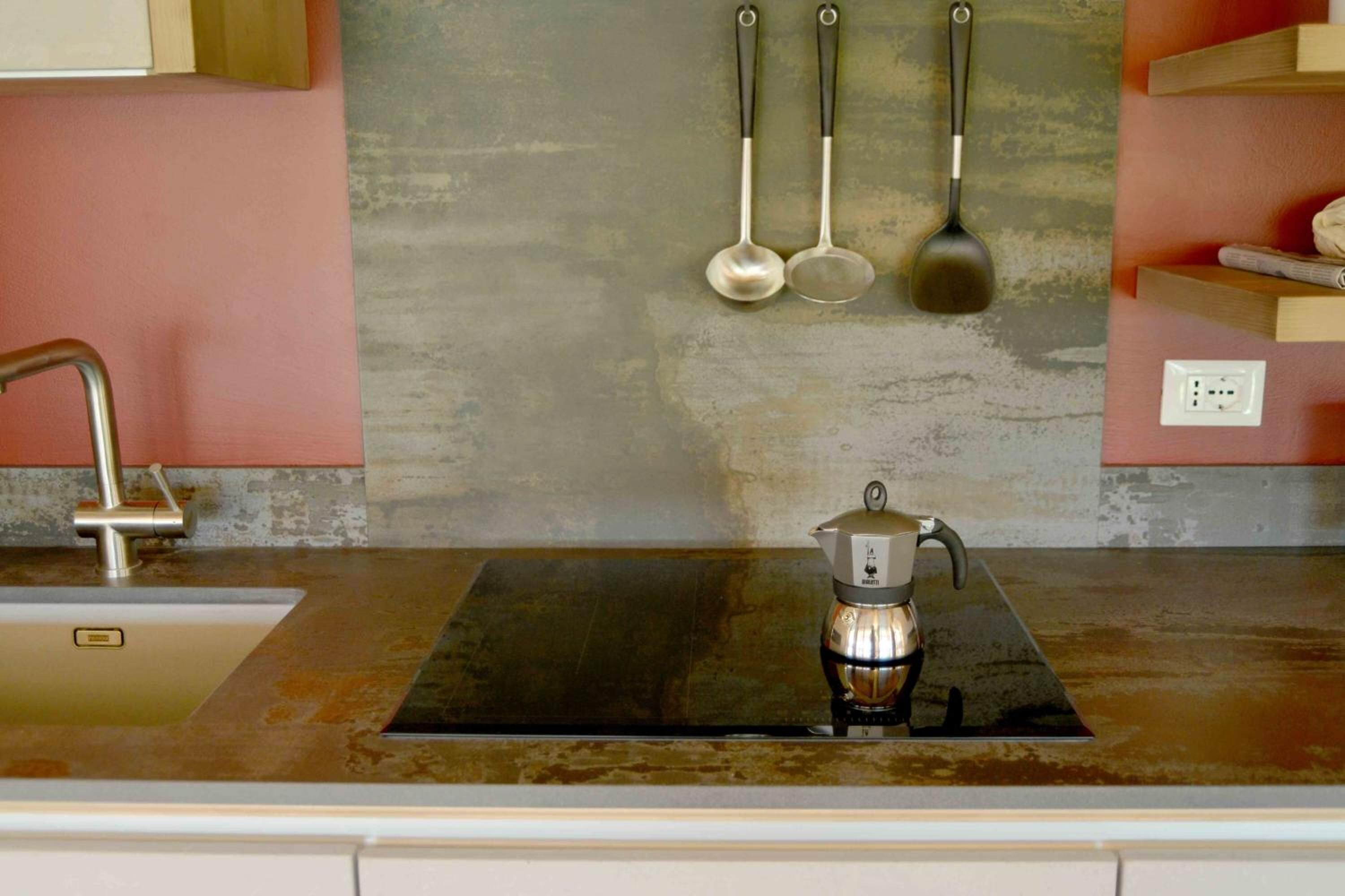 A kitchen with a stainless steel sink, a coffee maker, and hanging utensils.